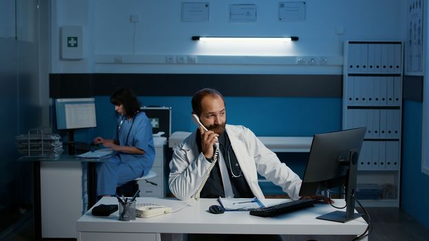 General practitioner answering landline phone having discussion with remote physician