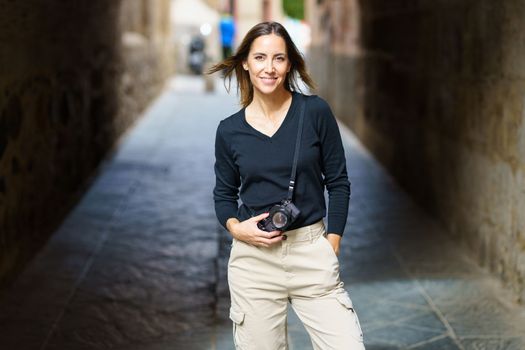 Smiling woman with photo camera looking at camera on narrow street