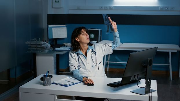 Physician holding radiography analyzing lungs expertise typing medical report on computer