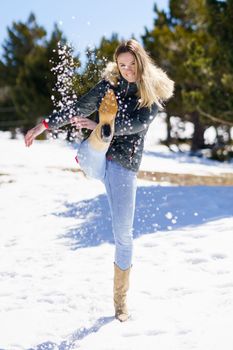 Young happy woman kicking snow in a snow-covered forest in the mountains