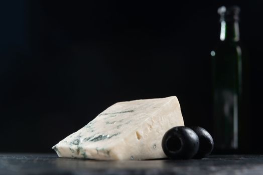 French cheese, roquefort with olives on plate, closeup. French Roquefort cheese with olives on a dark background. Moldy cheese with olives. Blue cheese on black background