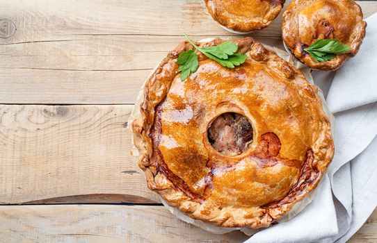Homemade meat pie with greenery on wooden background