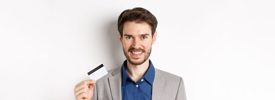 Shopping. Handsome candid business man in suit showing plastic credit card and smiling, recommending bank, white background