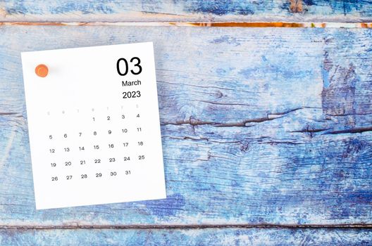 The March 2023 monthly calendar and wooden push pin on blue wooden background.