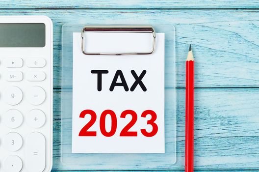 The Tax 2023 text on clipboard with calculator on wooden background. 2023 taxation concept.