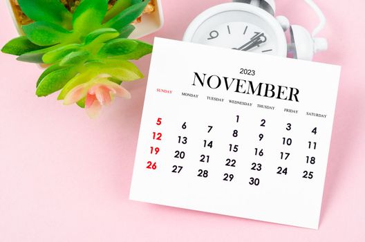 The November 2023 Monthly calendar for 2023 year with vintage alarm clock on pink colour background.