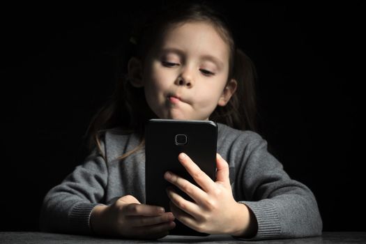 Kid girl with a thoughtful face at night communicates on Internet. Child gadget addiction and insomnia, psychological problems