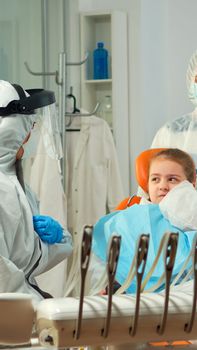 Child in protection suit showing dental problem to orthodontist