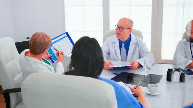 Woman doctor pointing on clipboard during briefing with coworkers