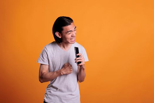 Man singing karaoke, grimacing, using smartphone as microphone