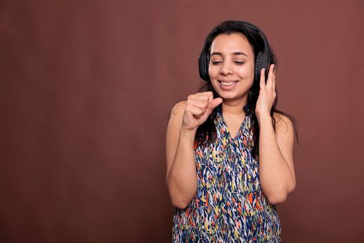 Smiling indian woman in headphones, singing in imaginable microphone