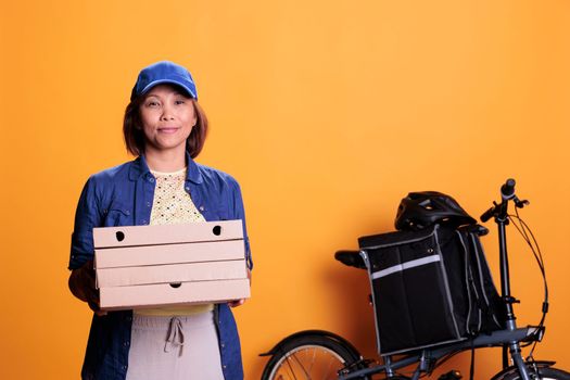 Asian takeout food delivery employee wearing blue uniform holding stack of pizza