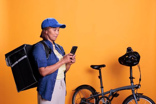 Elderly courier carrying takeaway food backpack checking directions and order details