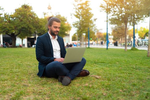 Handsome hispanic male businessman sitting lotus position in public park use laptop