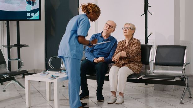 African american nurse talking to senior people in waiting room