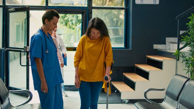 Medical assistant helping asian woman to walk with stick