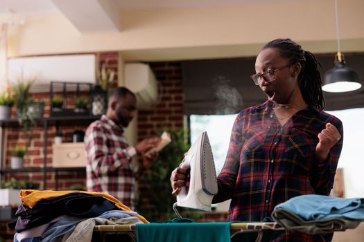 African american woman using steam iron at home.