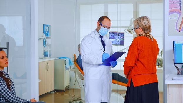 Orthodontist with mask speaking with elderly woman in waiting area