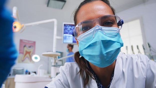 Pov of dentist working on patient mouth hygine in dental office checking teeth problems. Doctor examining in orthodontic office with light lamp and sterilized utensils, close-up face in medical mask.