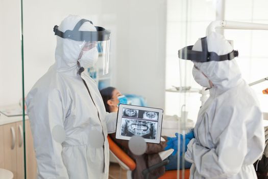 Dentist doctors with ppe suit analysing teeth x-ray using tablet