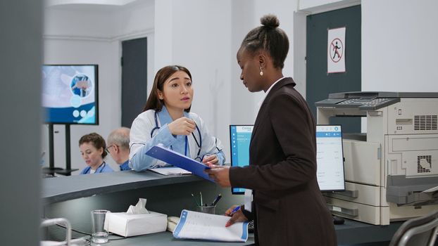 Diverse medical workers analyzing checkup papers at hospital reception desk