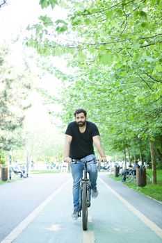 Young bearded man riding a bicycle in the park