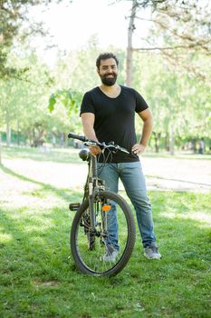 Relaxed man smiling to the camera while holding a bicycle