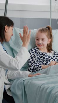 Pediatric woman doctor interacting with sick patient giving high five during clinical consultation