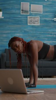 Athletic sport black woman doing morning fitness routine watching fitness workout video on laptop computer warming up before yoga class. Flexible adult training body muscle enjoying healthy lifestyle