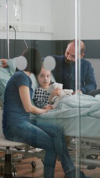 Worried parents sitting with sick girl daughter waiting for sickness expertise during medical examination