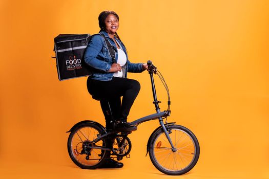 Portrait of fast food delivery worker riding bike during lunch time while carrying thermal takeout backpack