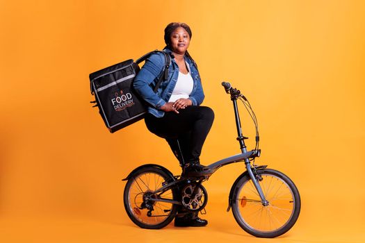 Pizzeria deliverywoman carrying food takeaway backpack while riding bicycle in studio