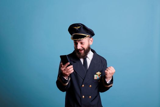 Happy excited airplane captain holding smartphone with winner gesture