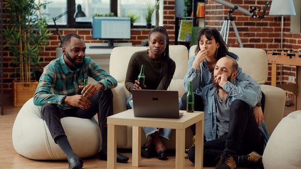 Diverse people watching video on laptop and talking at weekend hangout