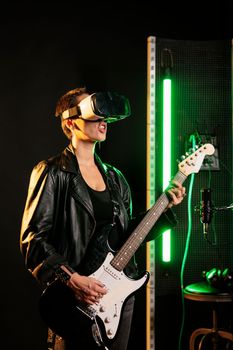 Woman performer playing at electric guitar in sound studio while wearing vr goggles for concert simulation