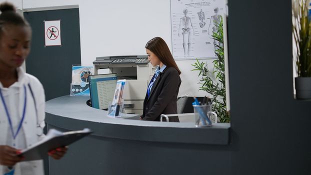 Asian receptionist using computer at hospital registration counter