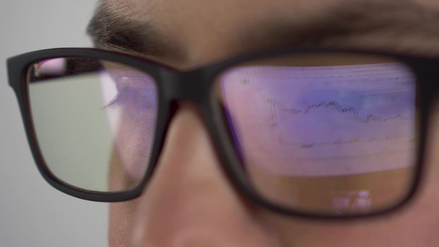 Reflection of the stock chart in glasses from the investor. A young man trades on the stock exchange and closely follows the chart. Glasses close-up.