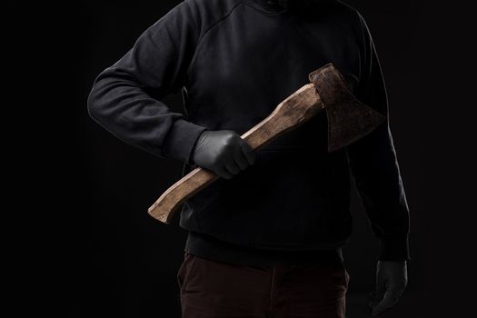 A man in gloves holds an ax in his hands against a black background