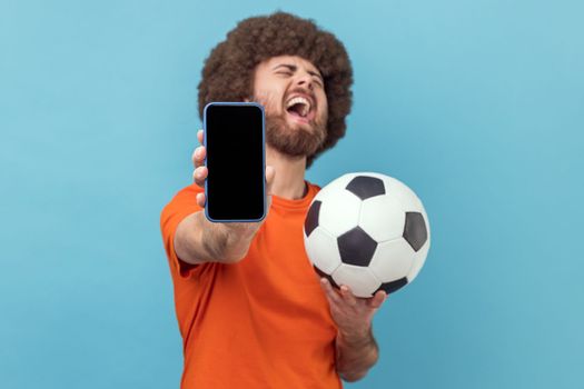 Man standing with soccer ball and showing mobile phone with empty display, betting and winning.