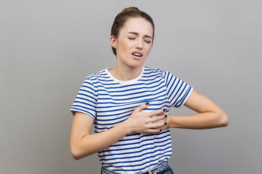 Woman clutching breast and grimacing from painful cramp, heart attack at young age, cardiac disease.
