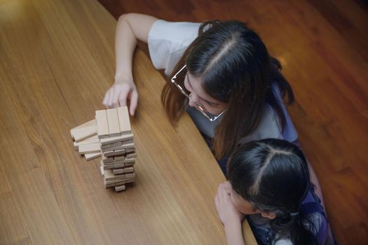 Asian young mother playing game in wood block with her little daughter in home living room