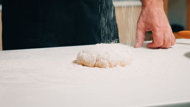 Hands of cook sprinkling flour on dough