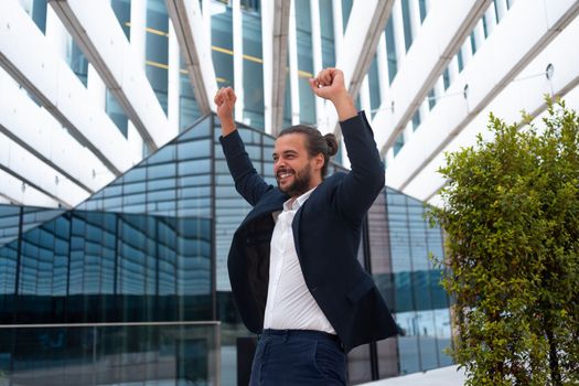 Excited young businessman in suit celebrating victory arms raised