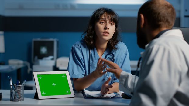 Assistant discussing patient expertise with medic while analyzing tablet computer with greenscreen template