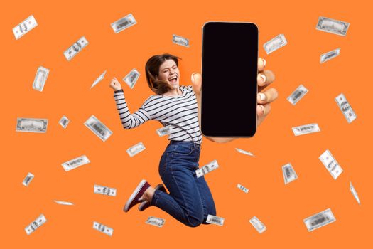 Woman jumping in money rain showing phone display with advertisement area, betting and winning.