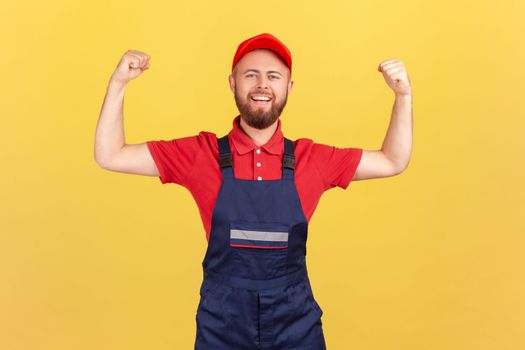 Worker man standing with raised arms and showing his power, looking at camera with pride.