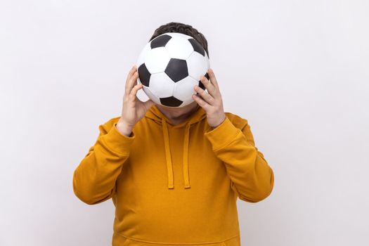 Anonymous unknown man hiding behind soccer ball, football fan covering his face during match.