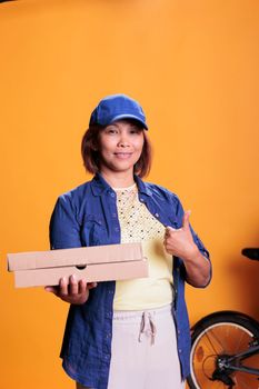 Smiling pizzeria delivery employee doing approval sign while delivering carton flatbox with pizza