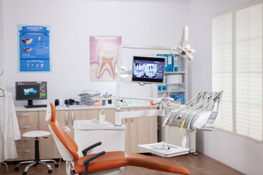 Dental chair and other accesorries used by dentist in empty cabinet. Stomatology cabinet with nobody in it and orange equipment for oral treatment.