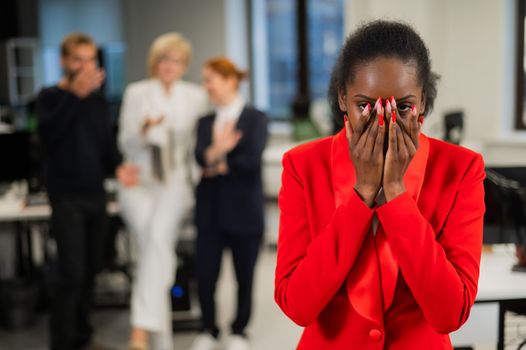 Young african woman crying because of the ridicule of colleagues. Racial discrimination in the office.
